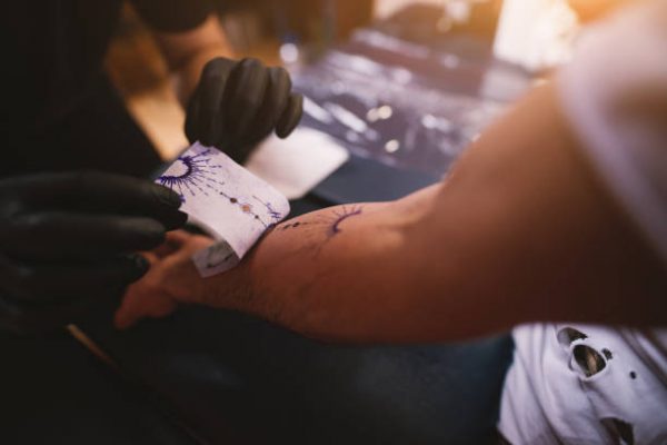 Close up of tattoo artists removing scetch sticker he previously made from customers arm.